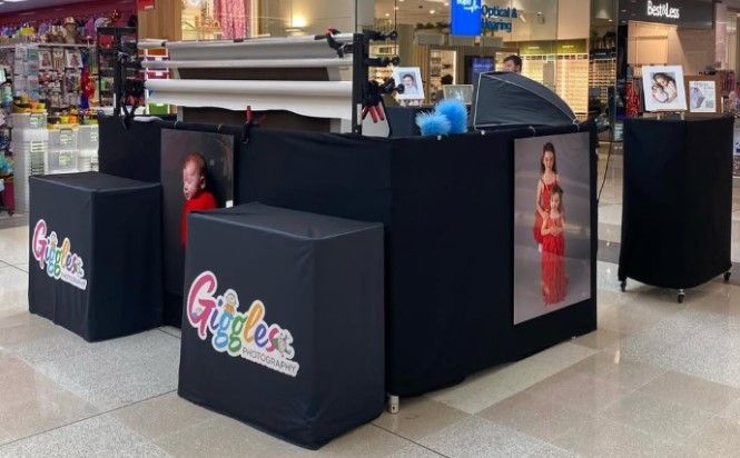 The Giggles pop-up booth in a shopping centre, with branded black cubes, photo backdrops and framed prints on display
