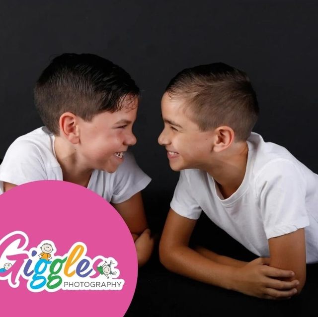 Two brothers in white t-shirts lying on a black backdrop, grinning at each other nose to nose