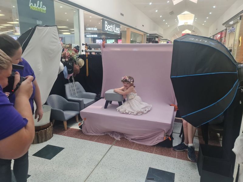 A little girl in a flower crown poses on a lilac backdrop while a Giggles photographer shoots at a shopping centre pop-up